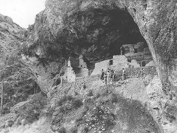 Black and white image of park ranger and visitors standing in front of the Lower Cliff Dwelling.