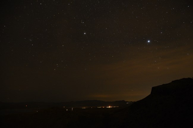 Lights from nearby homes and communities illuminates a star filled sky.