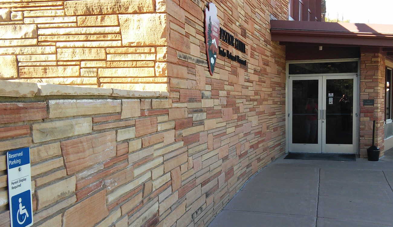 Entrance to Visitor Center in a brick wall. ADA parking sign displayed on left side of image.
