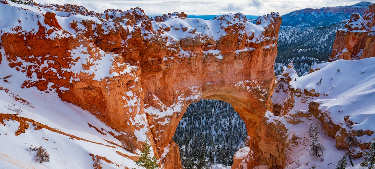 4+ hour winter banner A red rock formation in the shape of an arch covered in snow.