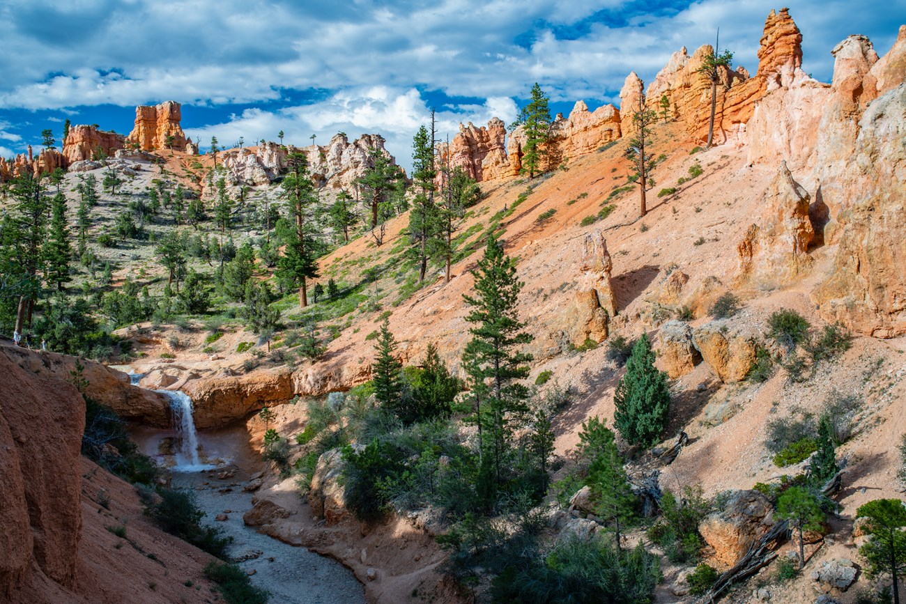 An overview of a stream flowing through red rocks with a waterfall in the distance