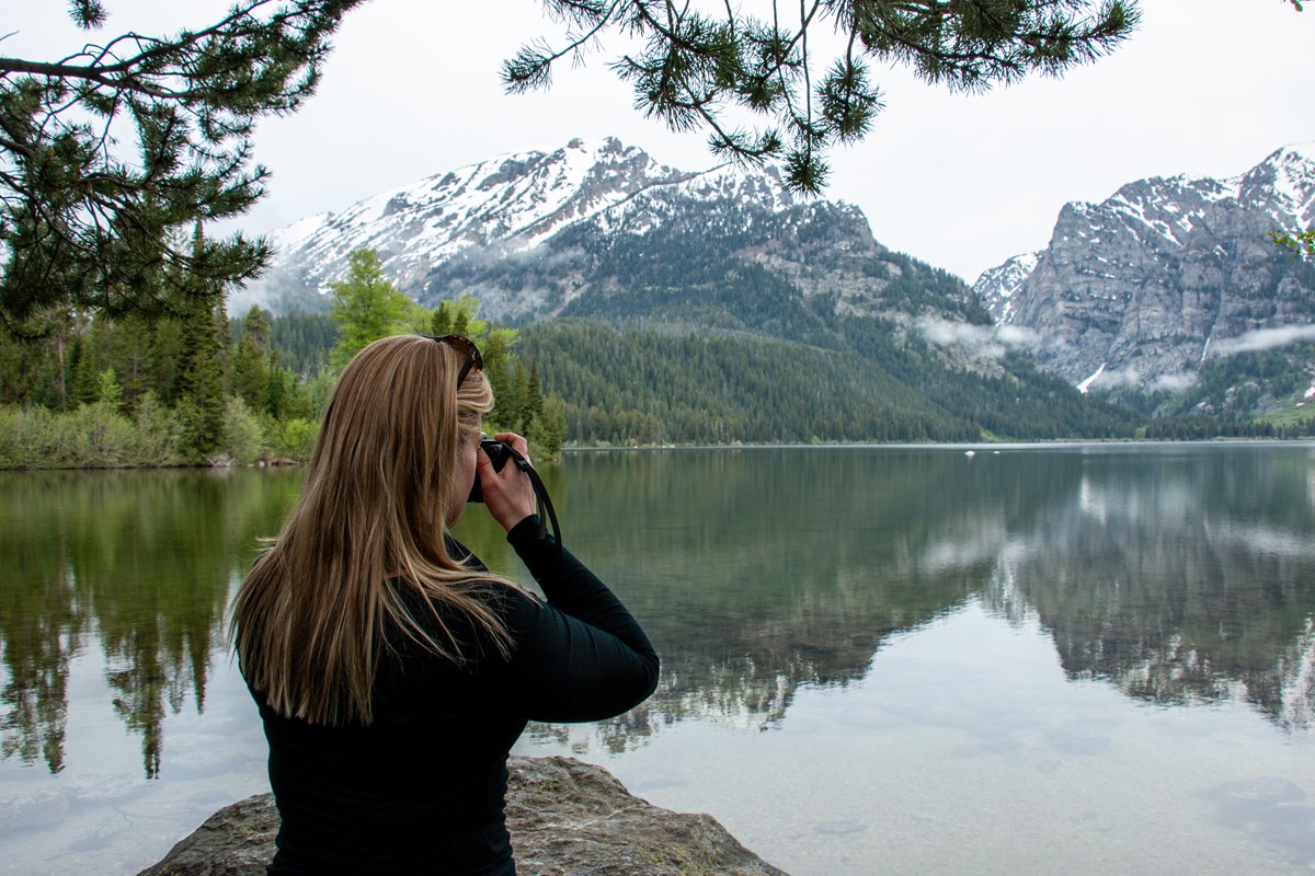Phelps Lake A woman takes a photo at a lakeshore.