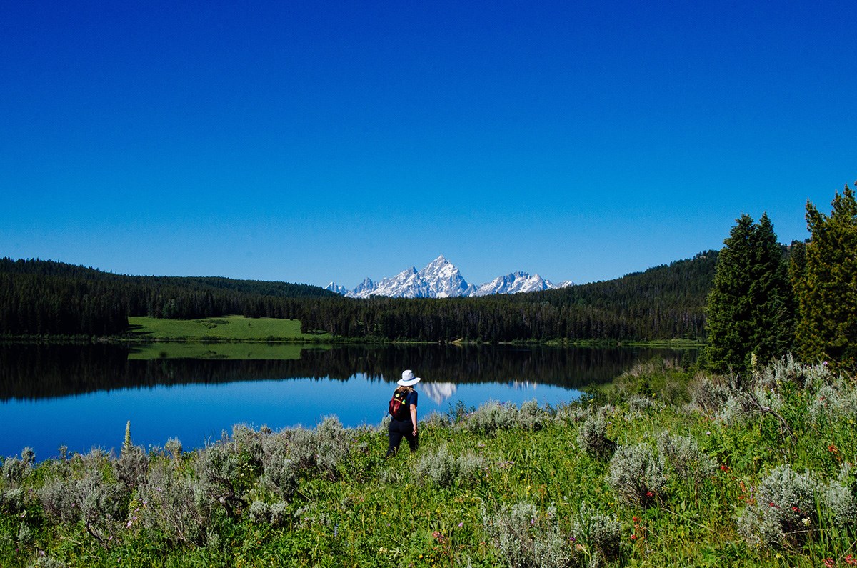 A hiker walks along a lakeshore towards mountains.