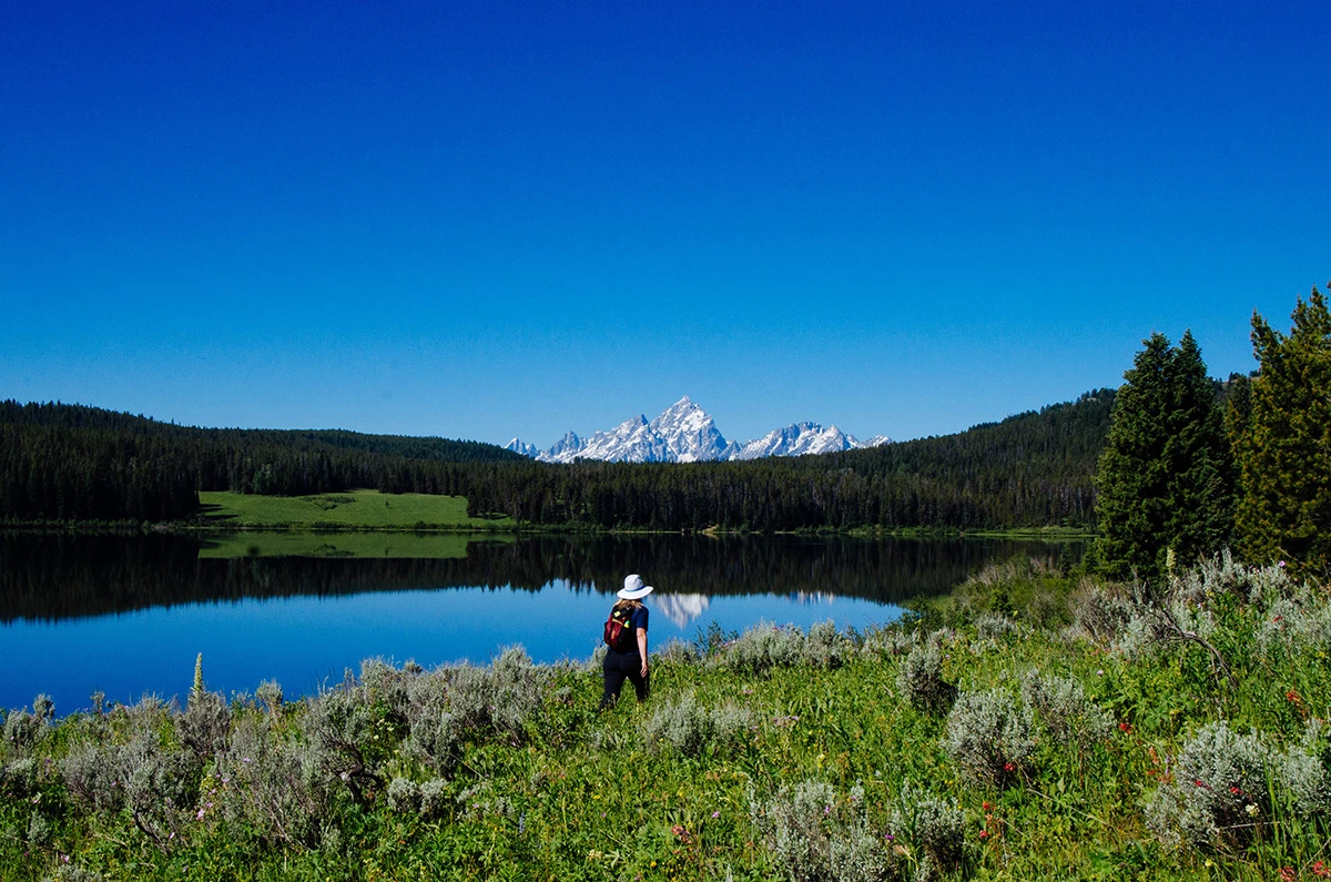 Two Ocean Lake A hiker walks along a lakeshore towards mountains.