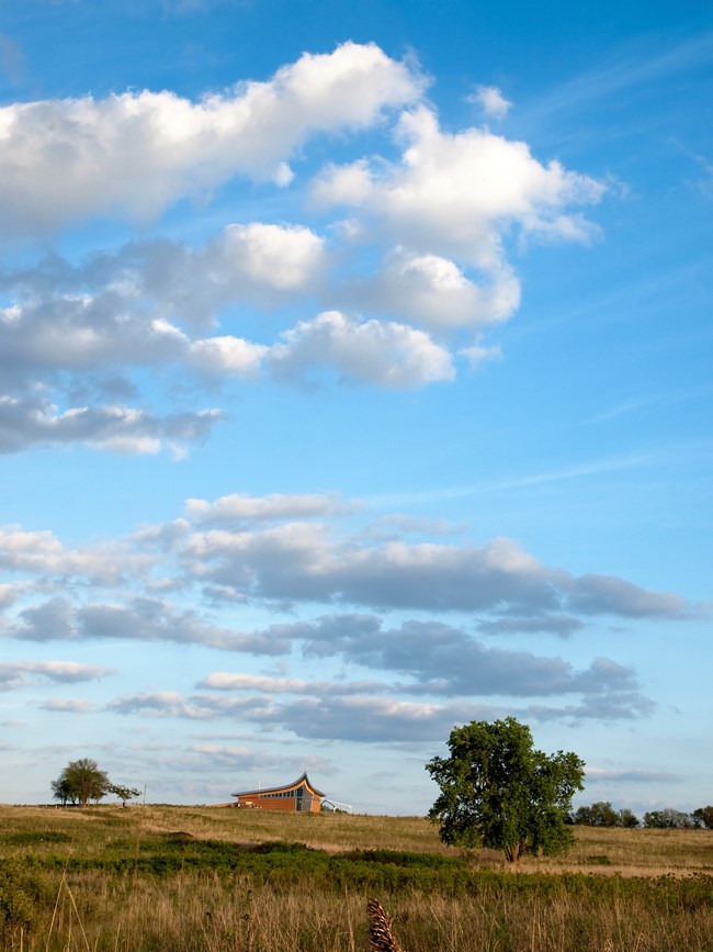 A blue sky with white puffy clouds over the prairie with the Heritage Center in the background.