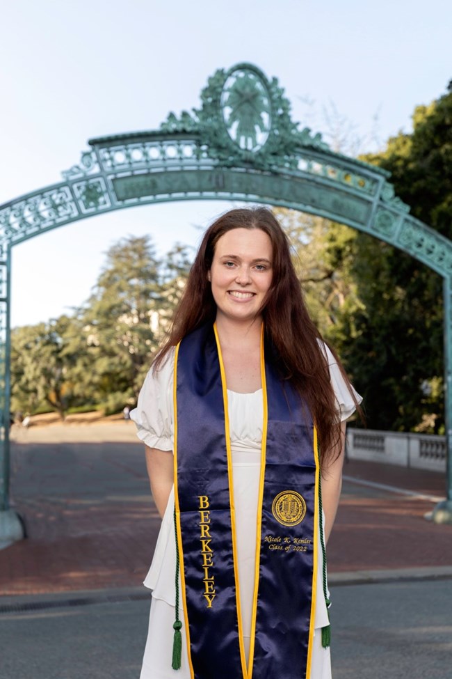 lt= A woman stands in her graduation regalia.