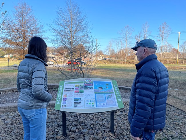People stand looking at an outside exhibit sign.