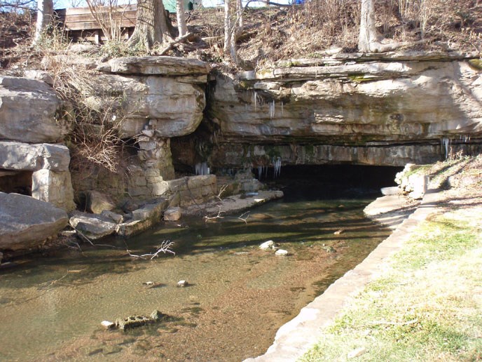 a spring surrounded by natural geologic rock and with the bottoms of trees showing at the top of the rock a spring surrounded by natural geologic rock and with the bottoms of trees showing at the top of the rock