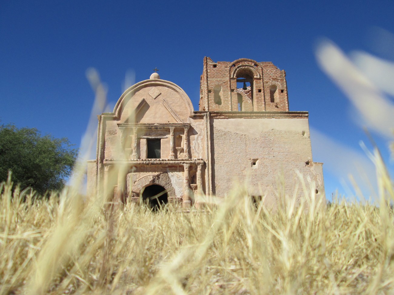 Photograph looking up to an adobe church from the ground with dry grass.