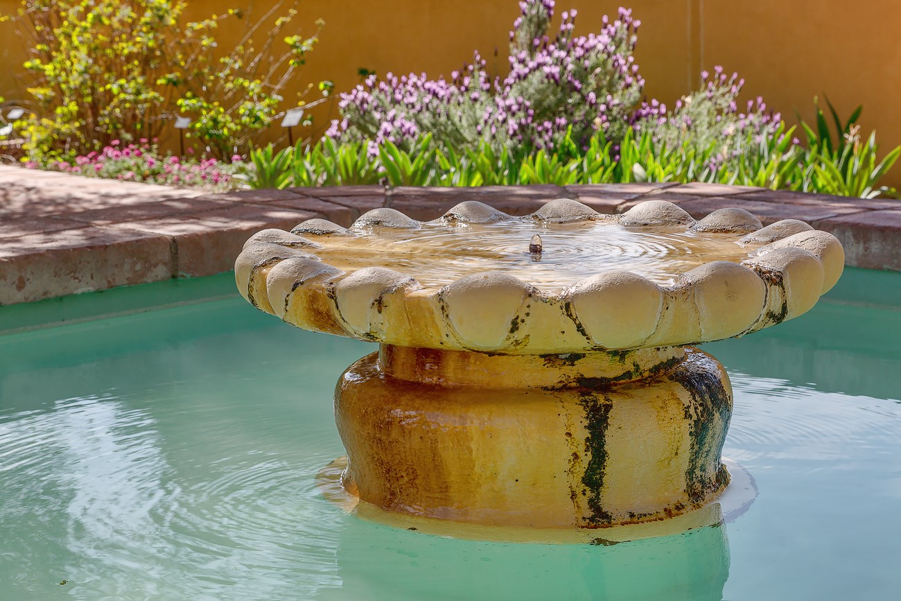 A stone water fountain surrounded by blooming flowers.