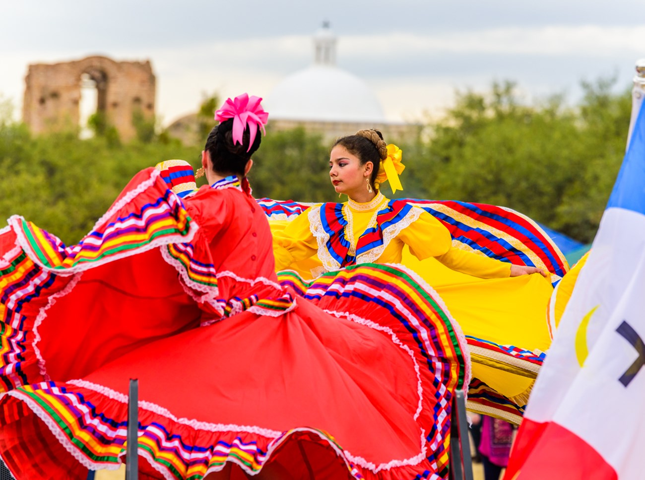 Dancers in colorful outfits dancing with church in background.