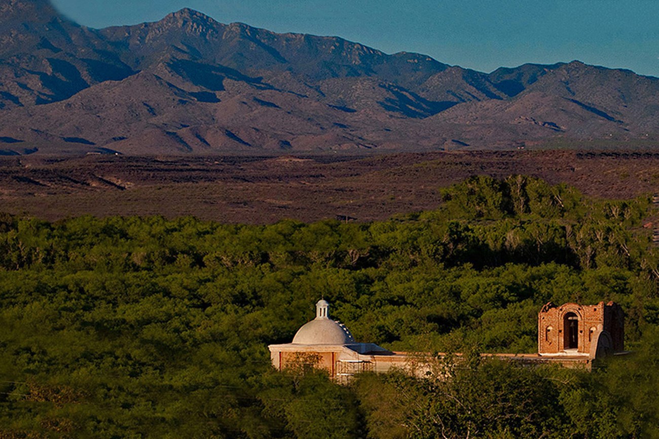 Landscape view of adobe church with mountains and foothills at sunset.