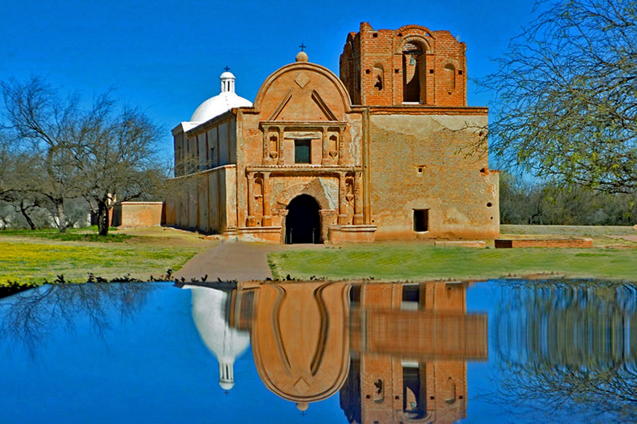Photograph of reflection of adobe church with church in background.