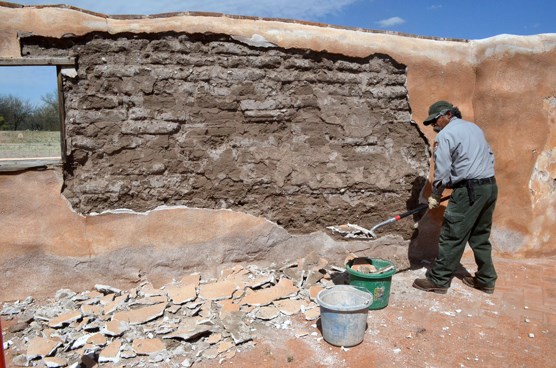 preservationist in front of exposed adobe wall with plaster and shovel
