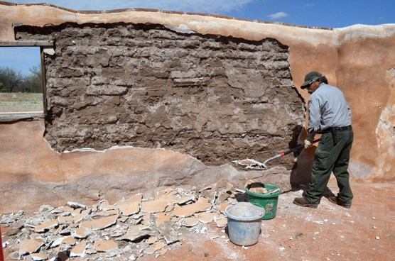 lt= preservationist in front of exposed adobe wall with plaster and shovel