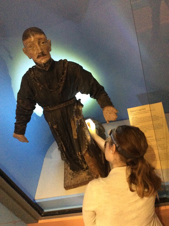 lt= preservationist examines wooden santo with headlamp