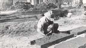 historic photo of man in cowboy hat bent over mud and adobe form