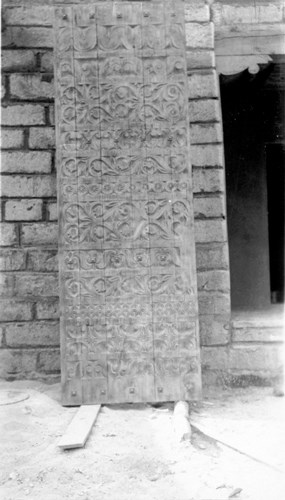 black and white photo of ornate carved door leaning against brick wall