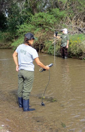 NPS staff with monitoring equipment standing in shallow riverbed
