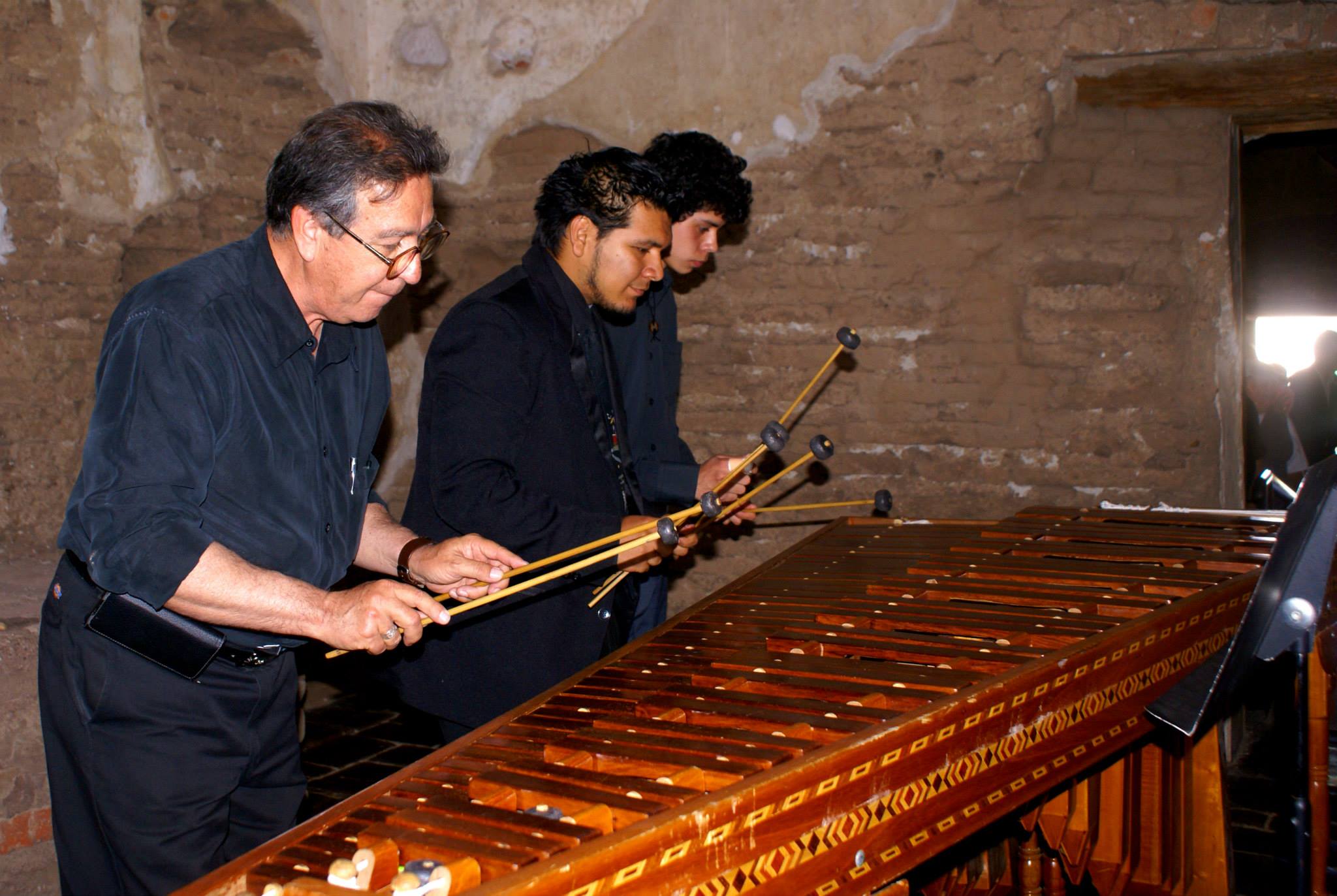 three men playing large marimba inside adobe church