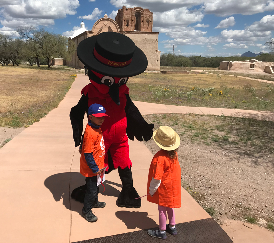 Pancho the Vermilion Flycatcher greets two young junior rangers in matching orange shirts.