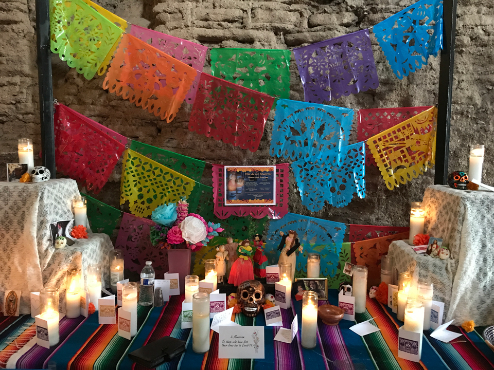 altar with papel picado, lit candles, offerings, notes, and other personal items