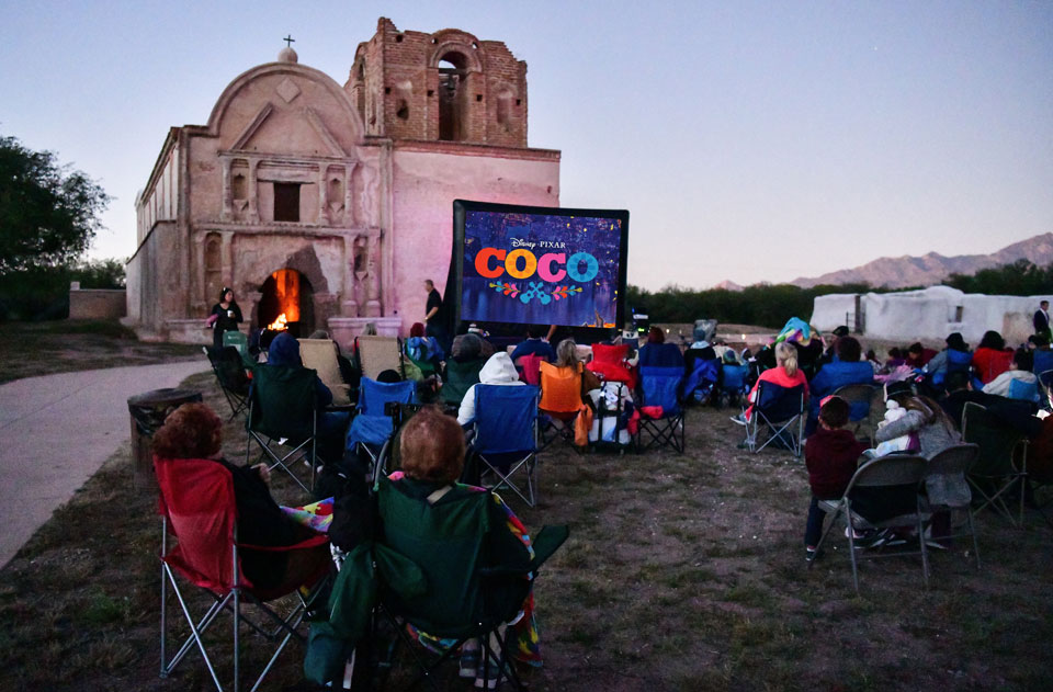 screening-with-coco-graphic visitors watching Coco on outdoor screen in front of church