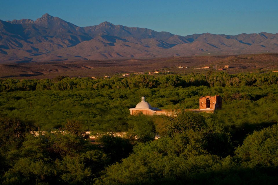 top of church peeking out over tree canopy with mountains in background top of church peeking out over tree canopy with mountains in background