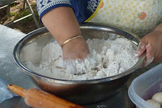 Flour tortillas-mixing Hands mixing flour, salt, lard, and water in a metal mixing bowl.