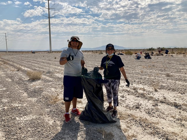 Two people pose with a black trash bag within a desert landscape