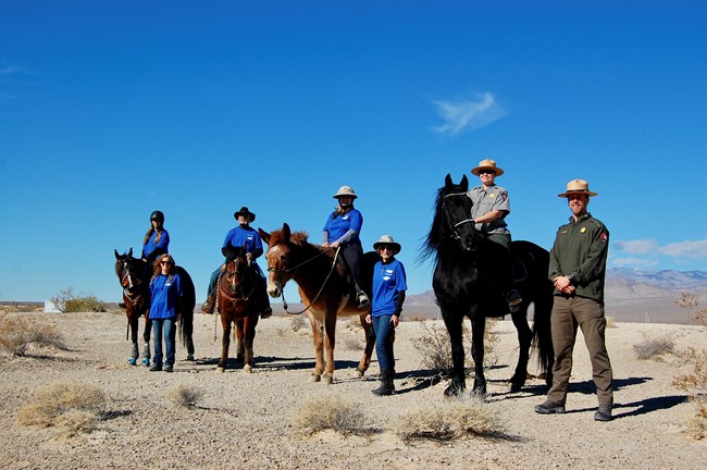 Four equestrians on horses, with volunteers and two park rangers in a desert landscape.