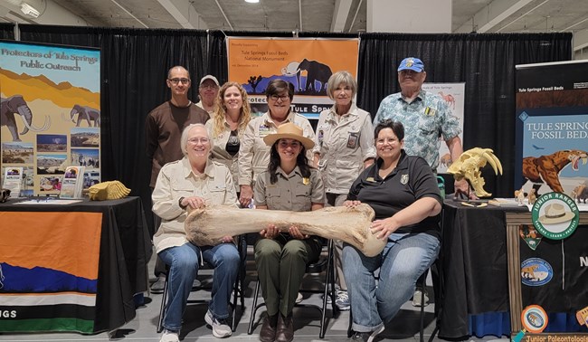 A group of volunteers and a park ranger pose with a replica of a mammoth thigh bone.
