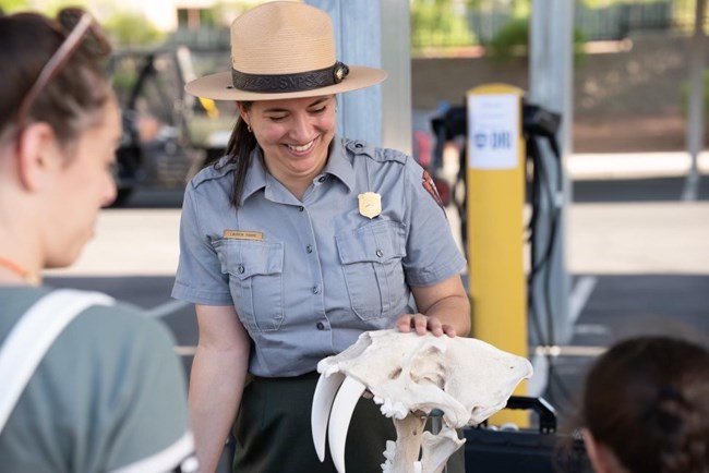 A park ranger laughing with a parent and child. She is holding a sabertooth cat skull