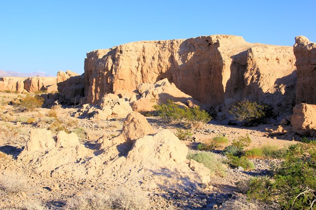 Tan badlands within a desert environment against a blue sky.