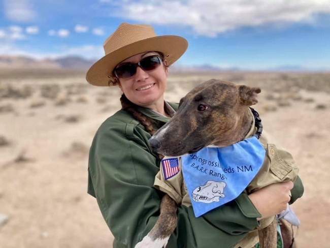 A park ranger holding her dog, who is wearing a B.A.R.K. Ranger bandana.
