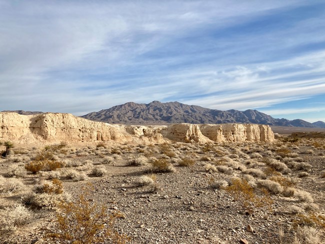 Sunlit badlands within a desert wash, surrounded by mountains