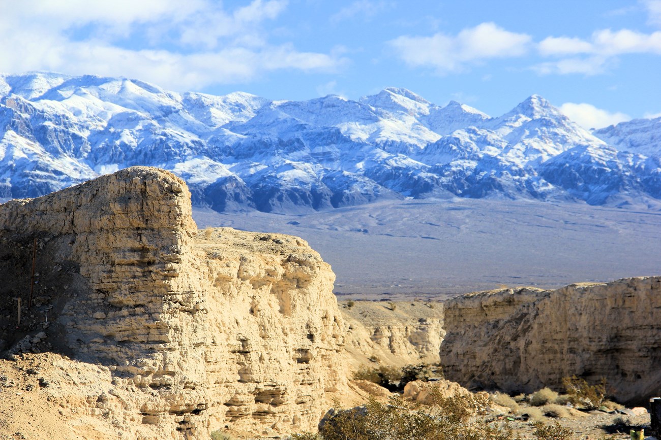 Tan badlands against a snowy mountain range.