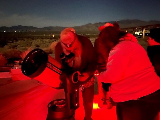 A volunteer assisting a visitor with using a telescope.