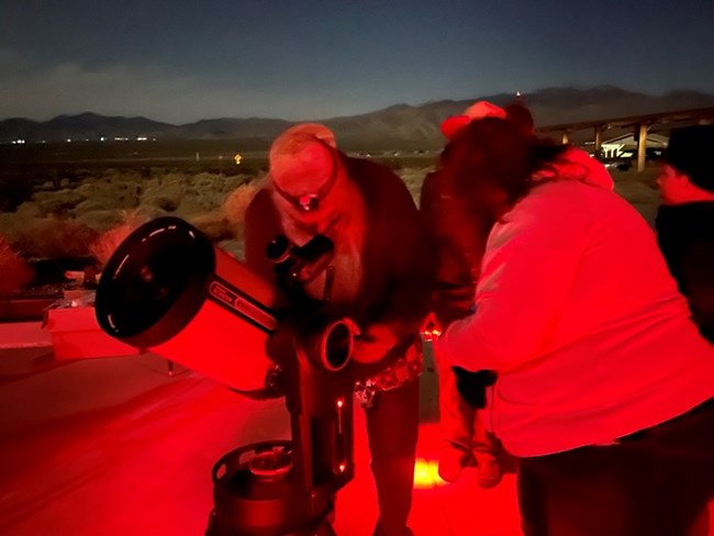 A volunteer assisting a visitor with using a telescope.