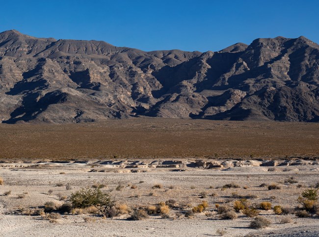 The badlands of a desert wash emerge below a moutnain range.