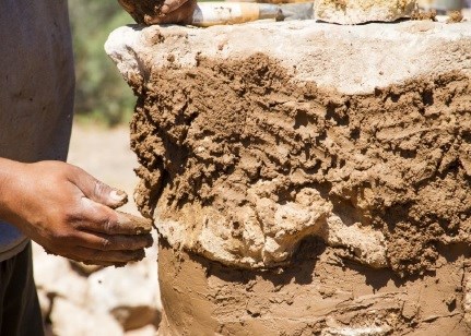 A hand applies masonry clay to the side of a stone built room.