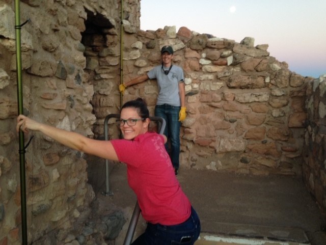 two people, one in a pink t-shirt and one in a green and grey NPS uniform, hold a net across the entryway to an old stone building