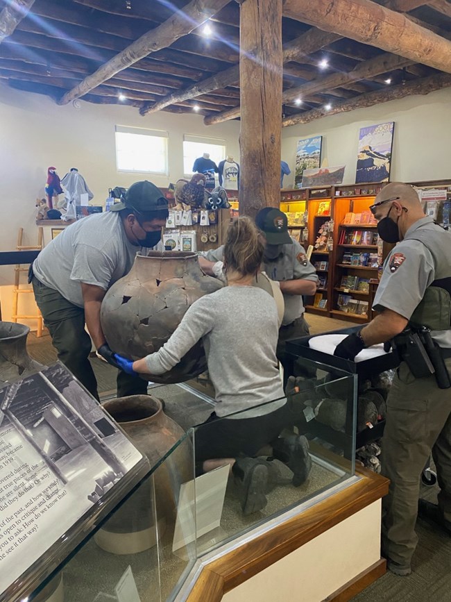 four uniformed park rangers moving a large olla from a display case onto a cart