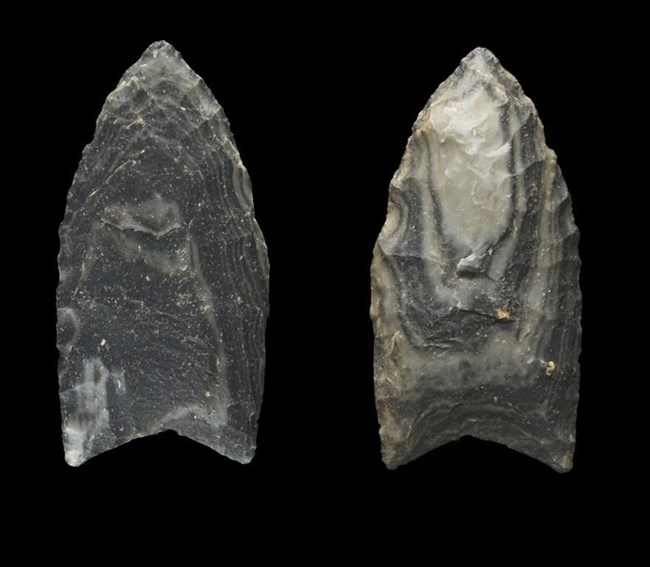 Two grey stone points on a black background. Both are pointed at the top and have a notch at the base. One is mostly solid grey, the other has stripes of light/dark grey