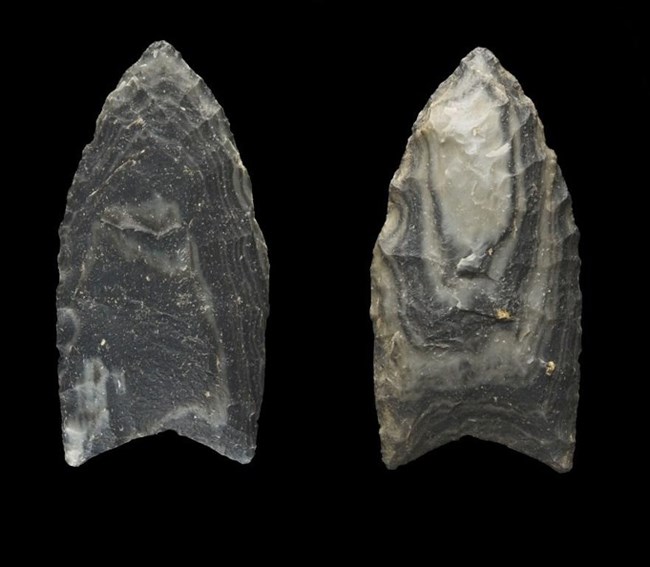 Two grey stone points on a black background. Both are pointed at the top and have a notch at the base. One is solid grey, the other has stripes of light/dark grey