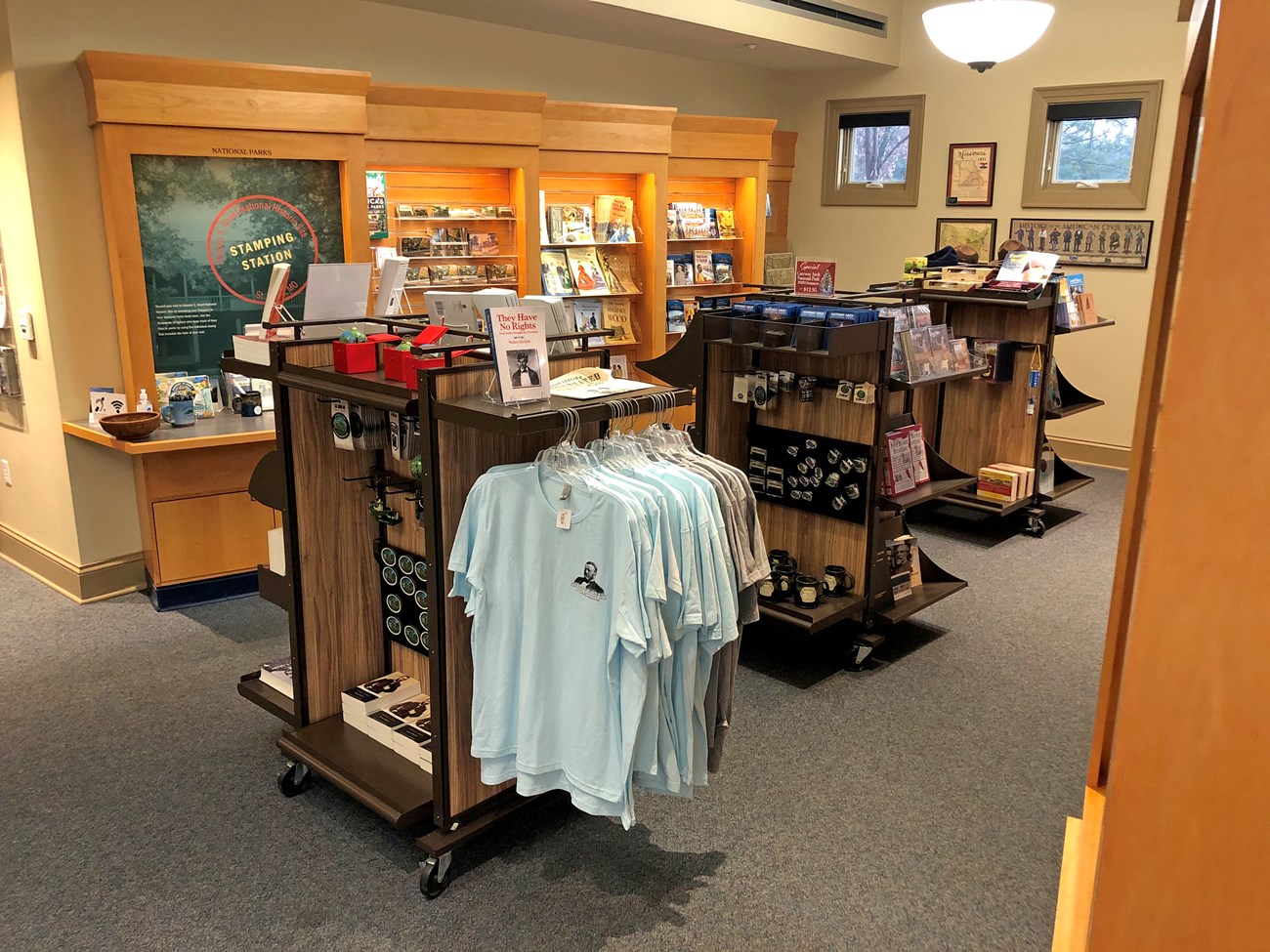 Tan wooden shelves containing books, ornaments, pins and t-shirts.