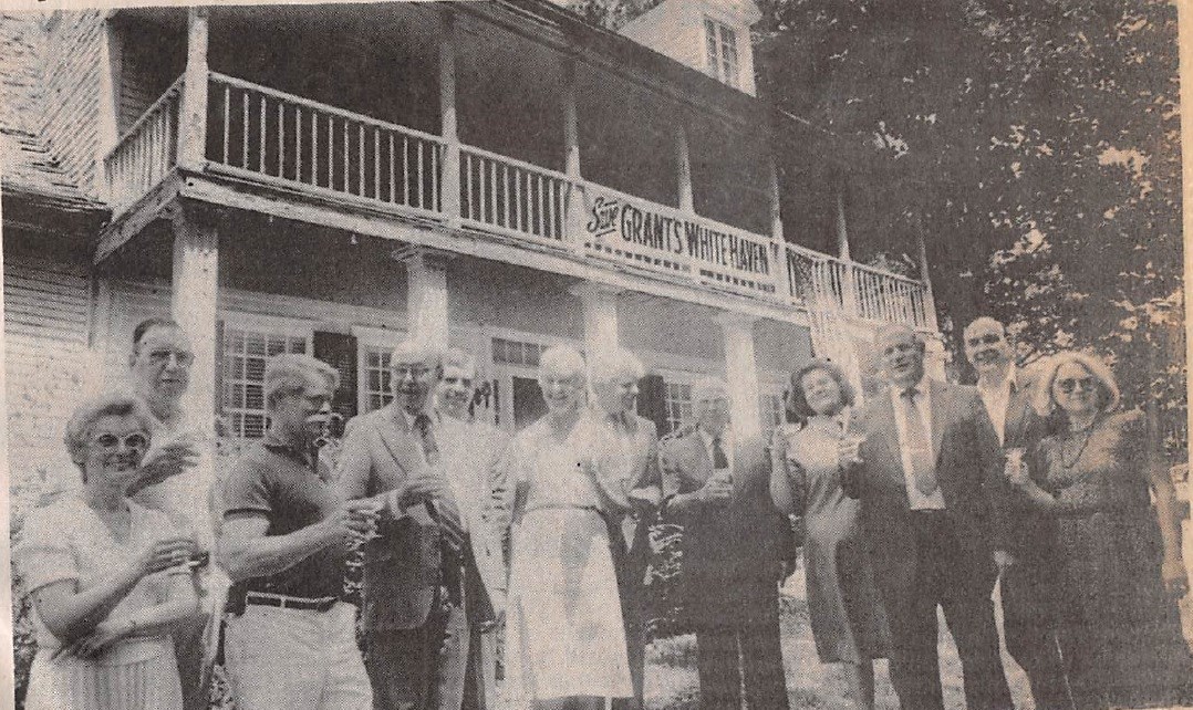Black and white photo of a men and women toasting in front of the White Haven home.