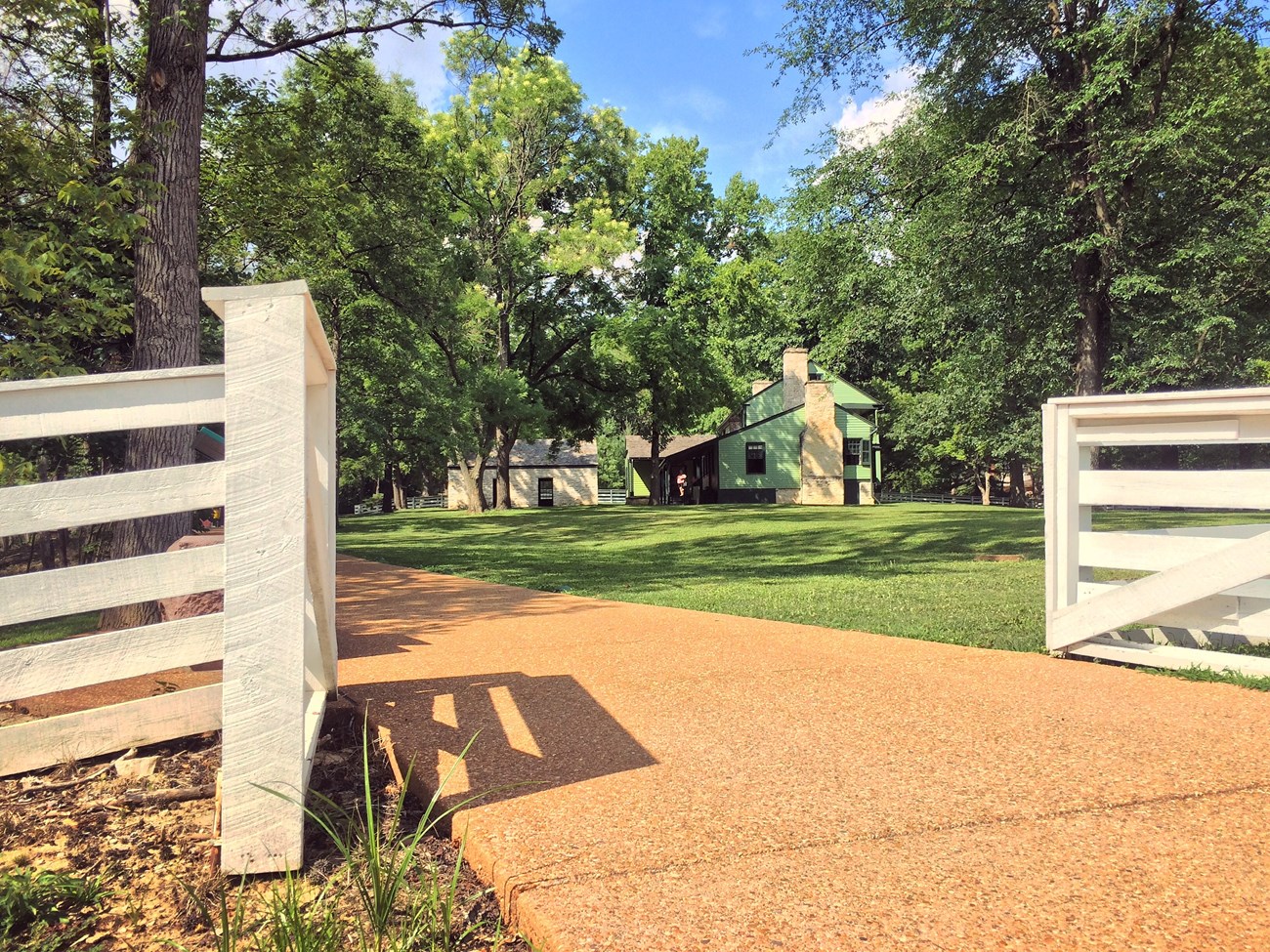 tan walking trace surrounded by white fence with green house in background.