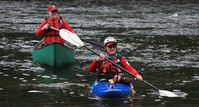 Two national canoe safety patrol volunteers paddle on the river in kayaks