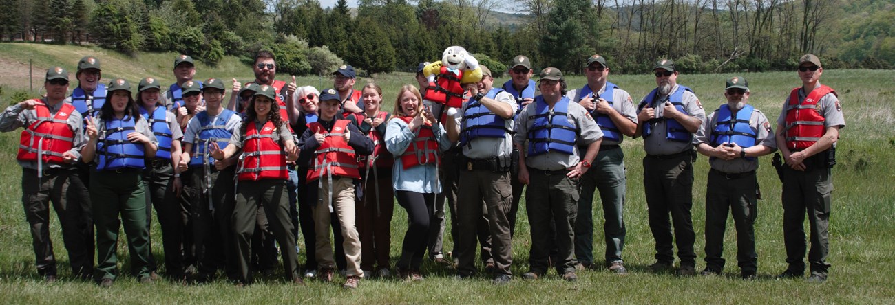 Group of 30-40 people, some in park ranger uniform, wearing life jackets and posing for camera